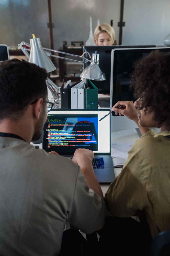 Home Two developers engage in software programming on a laptop in a modern office setting.